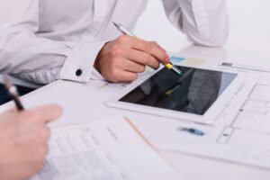 Una mano dibujando sobre un plano de arquitectura con un lápiz óptico en una tablet, simbolizando la fusión de la estrategia de negocio y la tecnología.